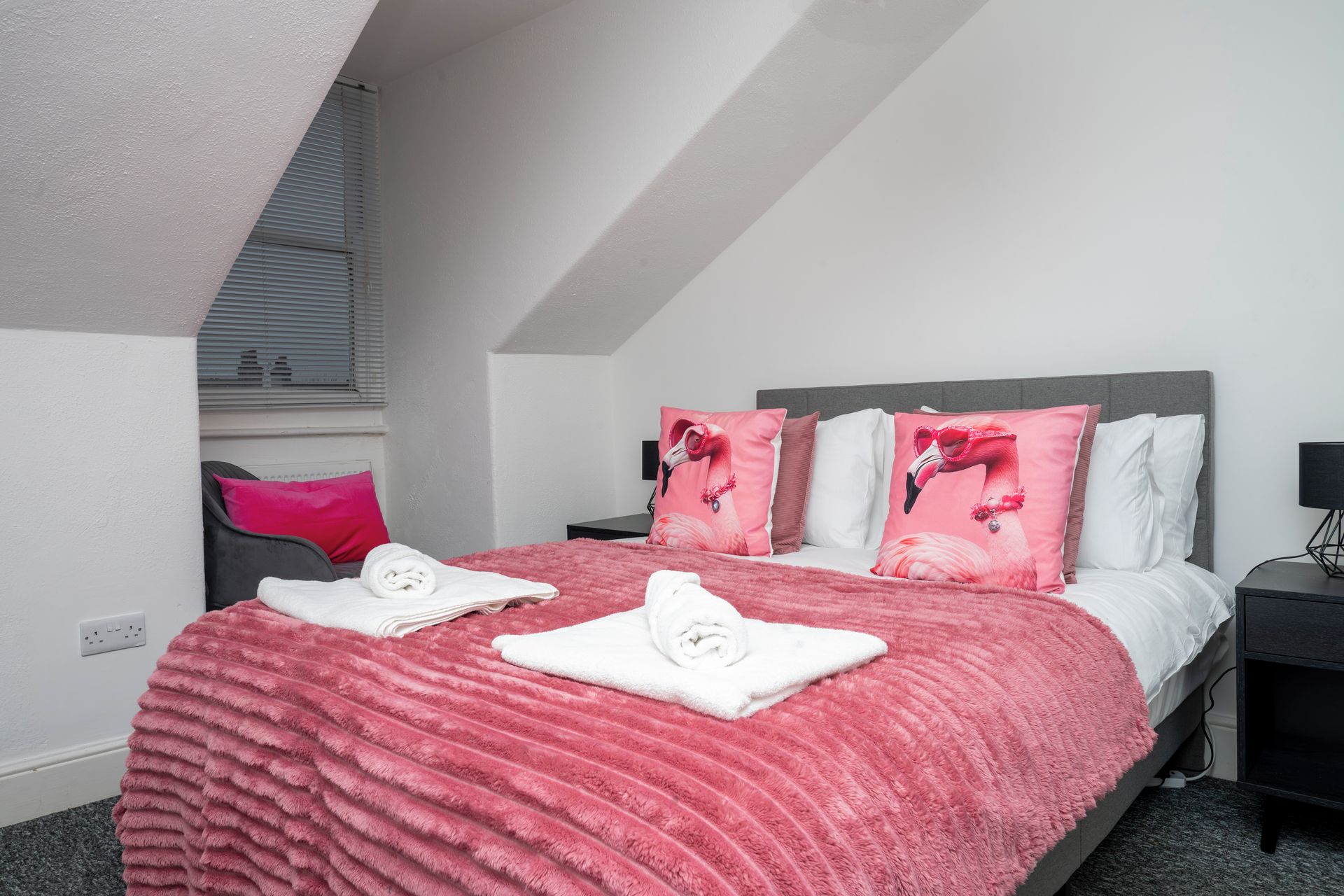 A bedroom with a bed, pillows, a blanket, a nightstand, and a lamp.