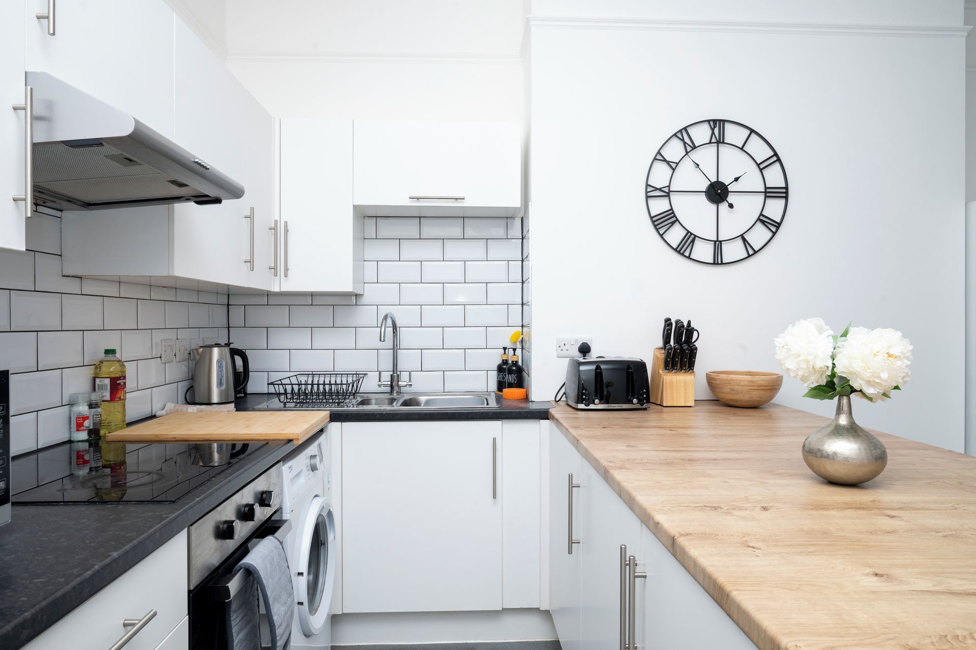 A modern kitchen with white cabinets, a stainless steel sink, a built-in washing machine, and a wooden countertop.