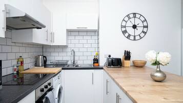 A modern kitchen with white cabinets, a stainless steel sink, a built-in washing machine, and a wooden countertop.