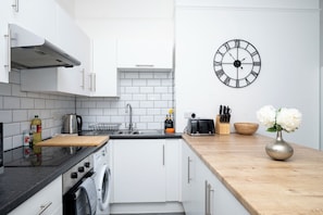 A modern kitchen with white cabinets, a stainless steel sink, a built-in washing machine, and a wooden countertop.