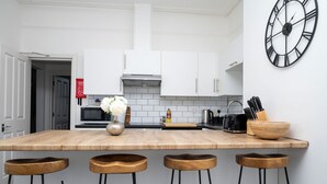 A modern kitchen with white cabinets, a wooden countertop, a black clock, and three wooden stools. - New Modern Boutique 4BDR Home in Central Brighton (Brighton and Hove)