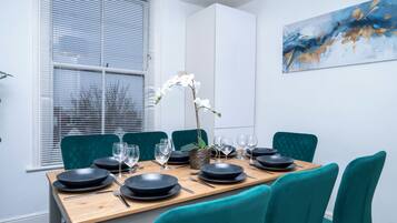 A dining area with a wooden table set for four, teal chairs, and a white orchid centerpiece.