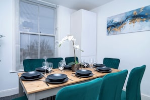 A dining area with a wooden table set for four, teal chairs, and a white orchid centerpiece.