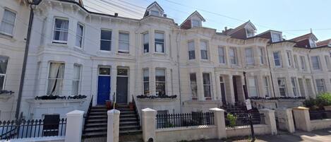 A row of white townhouses with a blue door, white railings, and a clear sky.