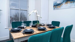 A dining area with a wooden table set for four, teal chairs, and a white orchid centerpiece. - New Modern Boutique 4BDR Home in Central Brighton (Brighton and Hove)