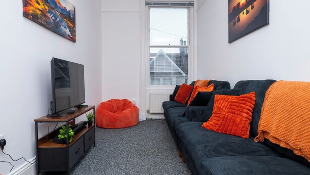 A modern living room with a flat-screen TV, a bean bag chair, a sofa with orange cushions, and two paintings on the walls. - New Modern Boutique 4BDR Home in Central Brighton (Brighton and Hove)