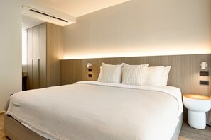 A modern hotel room with a large bed, bedside lamps, a toilet, and an air conditioning unit.