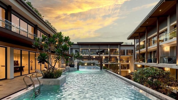 Un hotel moderno con piscina central, zona de estar exterior y vistas al atardecer.