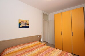 Un dormitorio con cama, mesita de noche, lámpara, armario y un cuadro en la pared.