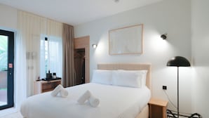 Ett hotellrum med en säng, ett nattduksbord, en lampa och utsikt genom en dörr.