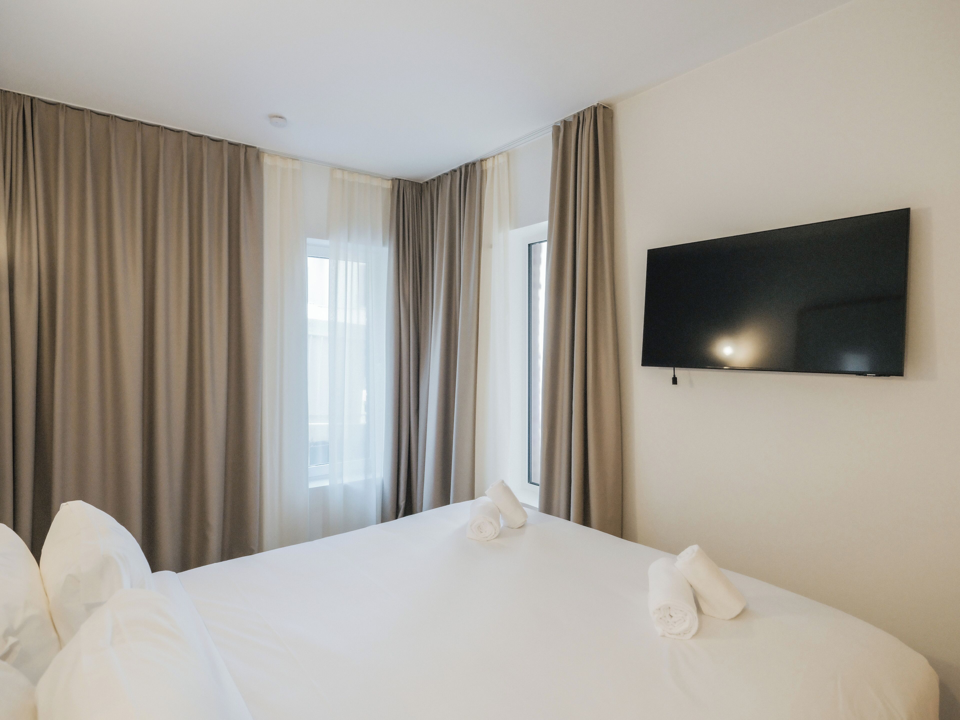 Hotellihuone, jossa on sänky, verhot, taulutelevisio ja ikkuna.