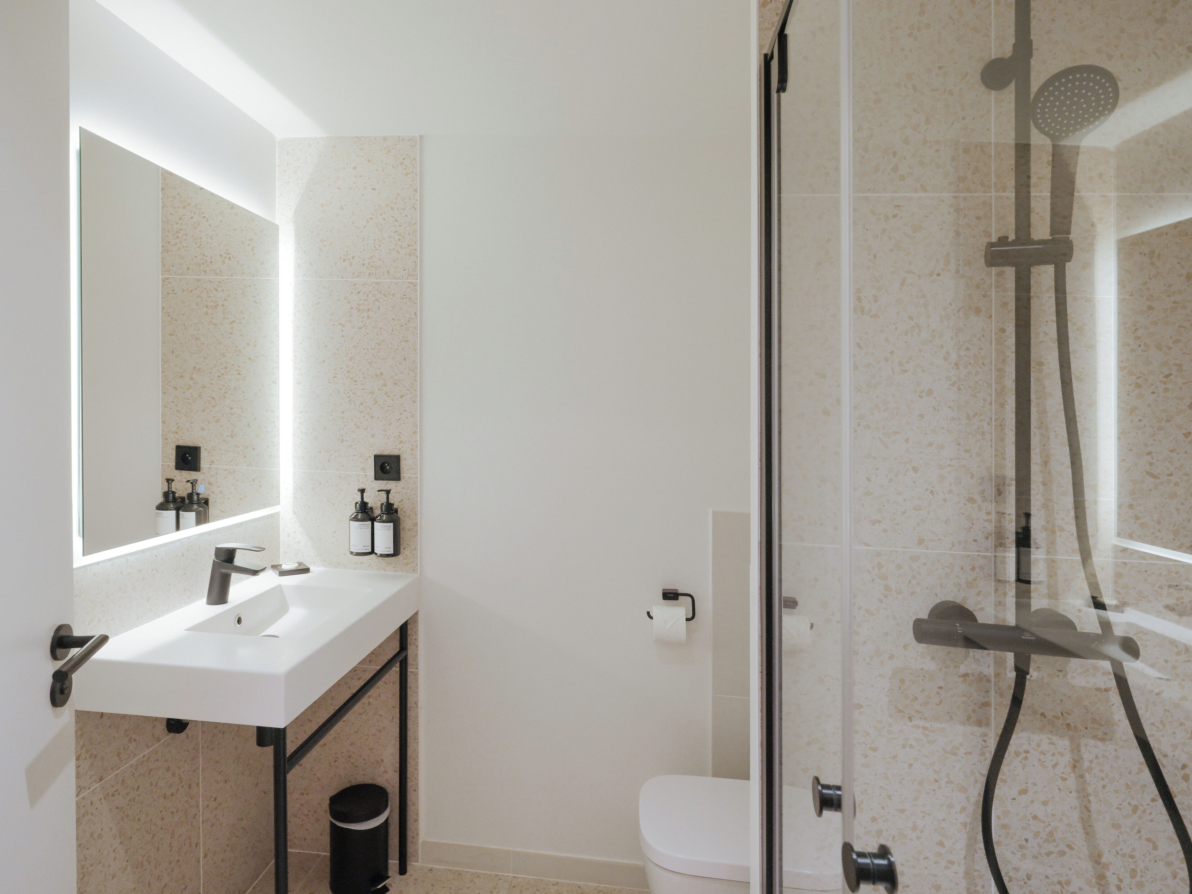 Een moderne badkamer met een douche met glazen wand, een witte wastafel en een spiegel erboven.