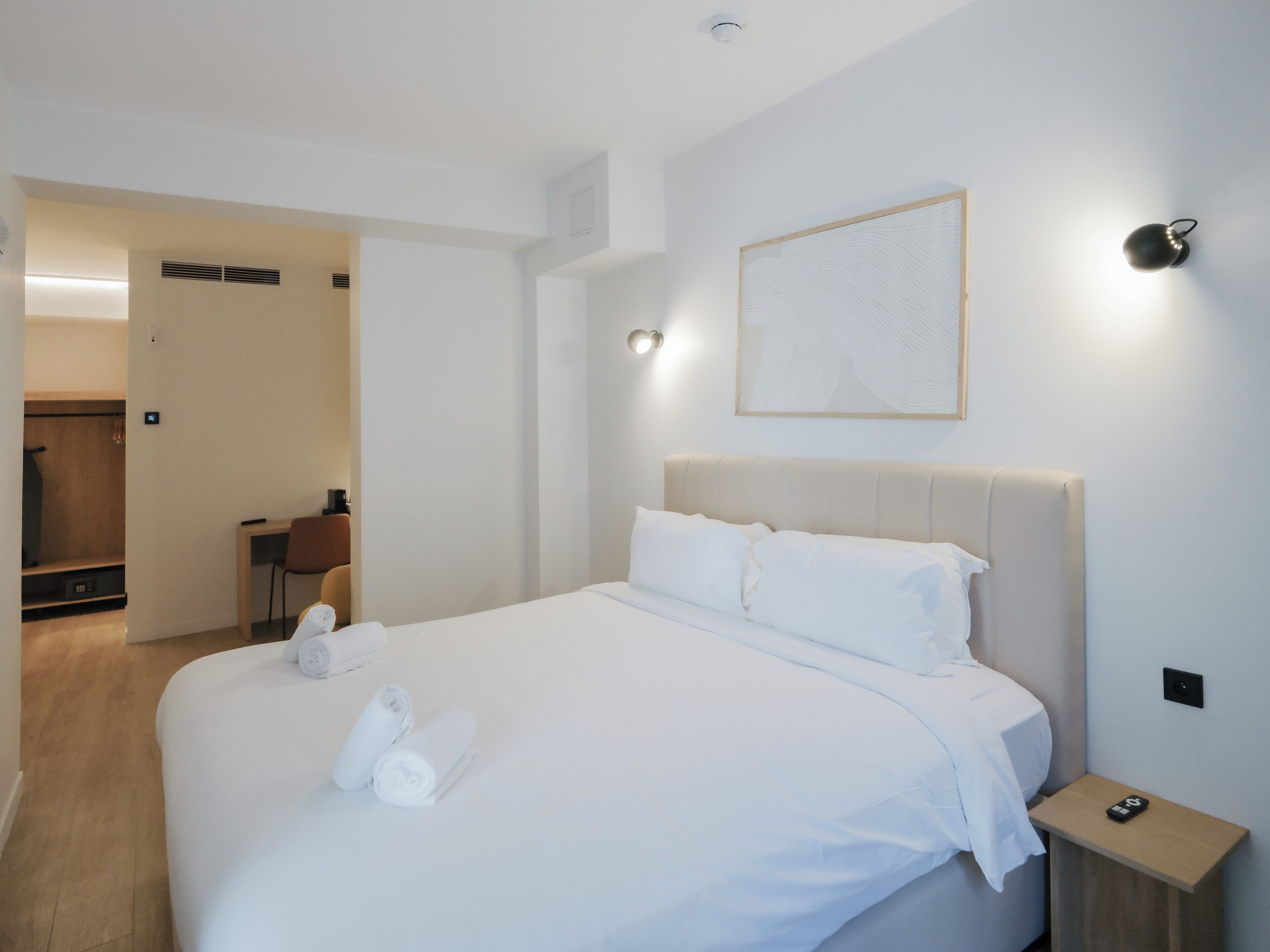 A hotel room with a large bed, a bedside table, a wall-mounted light, and a framed artwork.