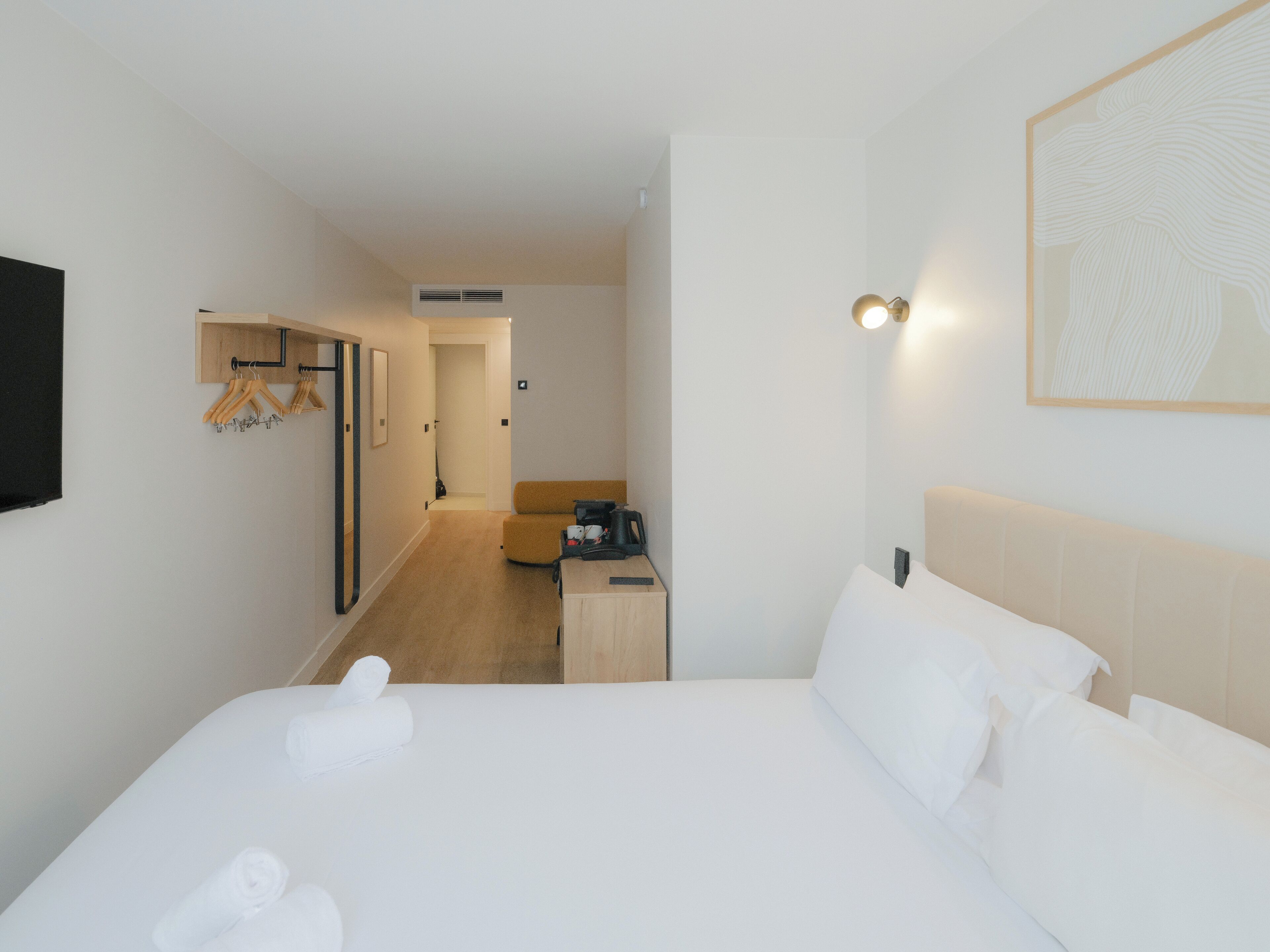 A hotel room with a bed, a desk, a chair, a television, and a coat rack.