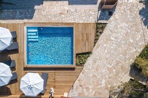 A rooftop pool with stone walls, wooden deck, and umbrellas. - PAGONA STUDIO (Rhodes)