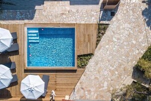 A rooftop pool with stone walls, wooden deck, and umbrellas.
