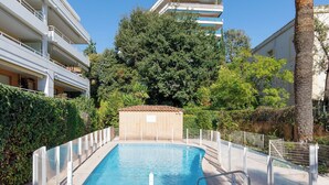 Ein rechteckiger Pool mit einer Metallleiter, umgeben von einem weißen Zaun, und ein Gebäude mit Balkonen im Hintergrund.