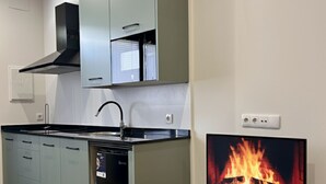 Ett modernt kök med gråa skåp, en svart köksfläkt, en diskmaskin och en tv-skärm som visar en bild av en öppen spis.