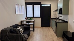 Ett kompakt bostadsutrymme med en soffa, ett litet bord, en liten köksdel och en dörr.