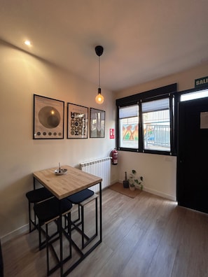 A room with a wooden table and chairs, framed artwork on the wall, a hanging light fixture, a window with blinds, and a door labeled 'SALIENT'. - CHA loft & Pool 08 (Salamanca)