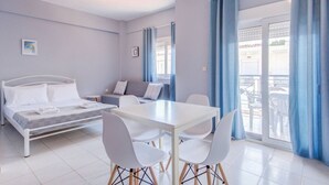 Een moderne hotelkamer met een bed, een bank, een eettafel met stoelen en een balkon met blauwe gordijnen.