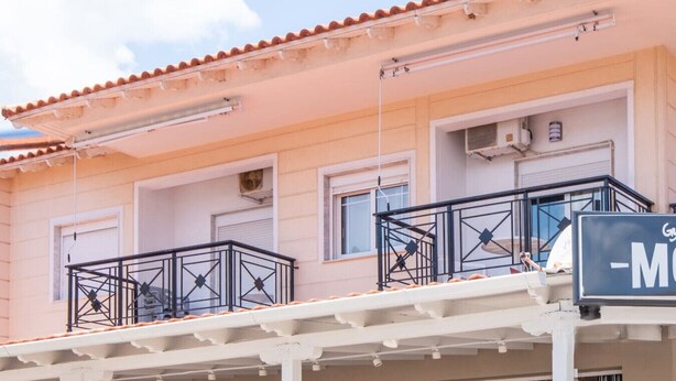 Een gebouw met een balkon en airconditioners, en een bordje met een gedeeltelijk zichtbaar stuk tekst 'Gry-M'.