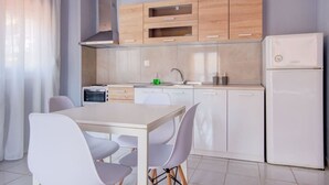 Een moderne keuken met houten kastjes, een ingebouwde oven, een spoelbak en een koelkast. Er staat een eettafel met stoelen.