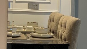 Un coin repas avec une table dressée pour quatre personnes, une chaise recouverte d’un tissu beige et, au-dessus de la table, un tableau abstrait encadré.