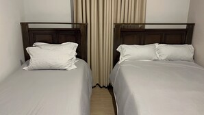 Deux lits simples avec des têtes de lit en bois, une literie blanche et un rideau servant de séparation dans une chambre d’hôtel.