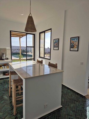 A modern kitchen with a large island, two windows with views, and a hanging light fixture. - Villa Akwaba magnificent country house (Essaouira)