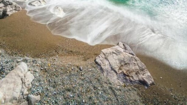 Paesaggio costiero con acque turchesi cristalline, una formazione rocciosa imponente e una spiaggia sabbiosa.