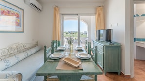 A dining area with a table set for four, a sofa, a television, and a view through a glass door. - Dreamy apartment in Orosei (Orosei)
