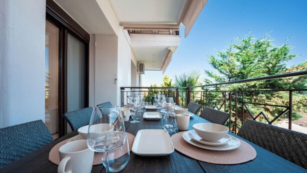 Ein Balkon mit Esstisch, Gartenmöbeln und Blick ins Grüne.