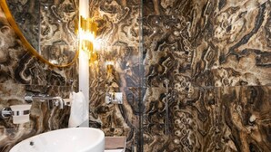 Ein Badezimmer mit Marmorwand, einem weißen Waschbecken und einer Glasdusche.