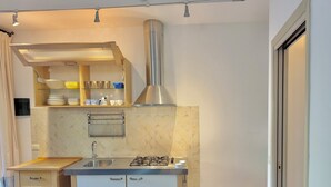 Cuina compacta amb fogó de gas, rentamiques d'acer inoxidable i forn integrat. Hi ha un taulell de fusta i un petit armari amb una barra penjant per a tovalloles.