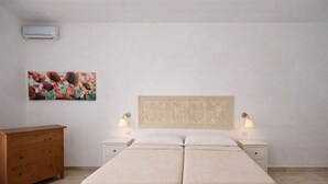 Un llit doble amb capçalera, dues taules de nit amb làmpades, un aparador de fusta i un quadre floral a la paret.