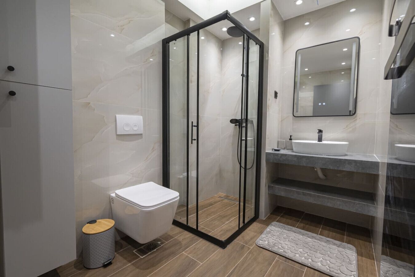 A modern bathroom with a glass-enclosed shower, a white toilet, and a vanity with a mirror.