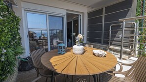 Et rundt træbord med stole, en lygte og en vase med blomster på en balkon med udsigt.