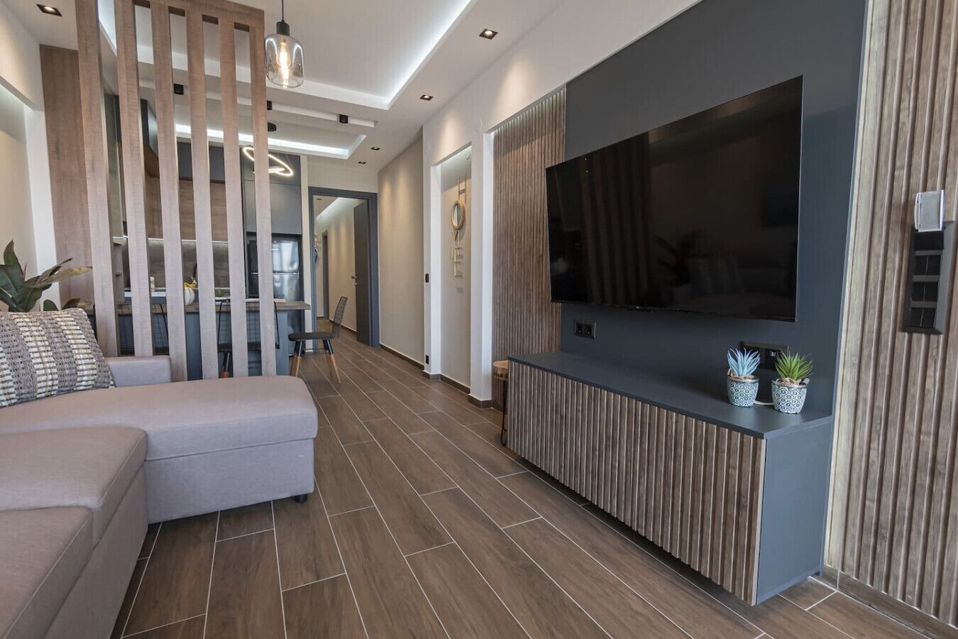 Ein modernes Wohnzimmer mit großem Flachbildfernseher, einer Couch, einer Wand im Holzdesign und einem Blumentopf.