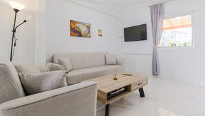 Uma sala de estar moderna com sofá, mesa de centro, obras de arte, TV e uma janela com cortinas.