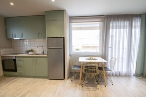 A compact kitchen with a built-in oven, a refrigerator, and a dining area with a table and chairs. - Marianthi Seaview Loft by RentalsPro (Nea Moudania)