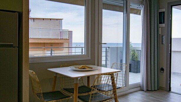 Ein Balkon mit Tisch und Stühlen, Blick auf das Meer und ein Gebäude im Hintergrund.