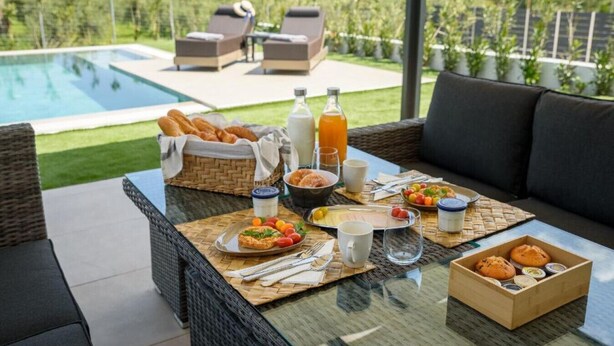 A dining area with a pool view, wicker furniture, and a breakfast spread. - Topaz 2 Bedroom Suite with Private Pool (Pefkochori)