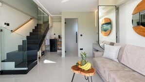 Een moderne woonkamer met een trap, een bank, een salontafel met fruit en een grote spiegel.