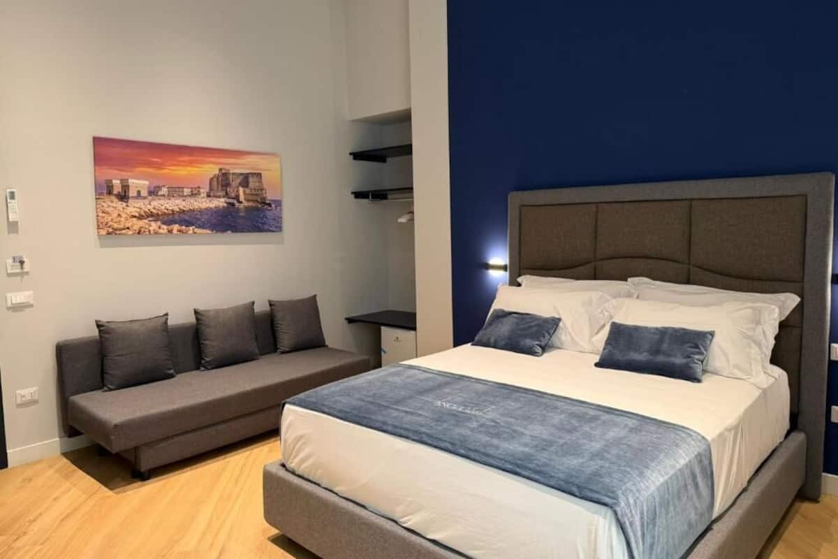 A bedroom with a bed, a sofa, a painting, and built-in shelves.