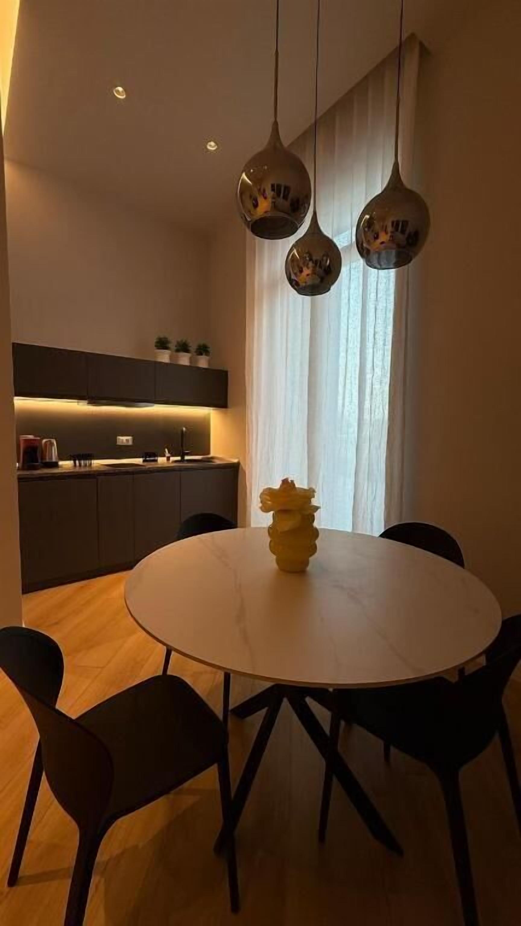 A modern dining area with a round table, four chairs, and a vase of flowers.