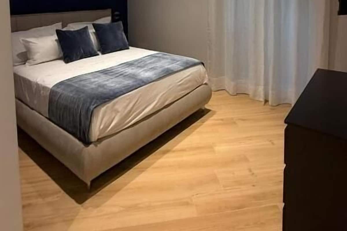 A modern bedroom with a bed, curtains, and a wooden floor.