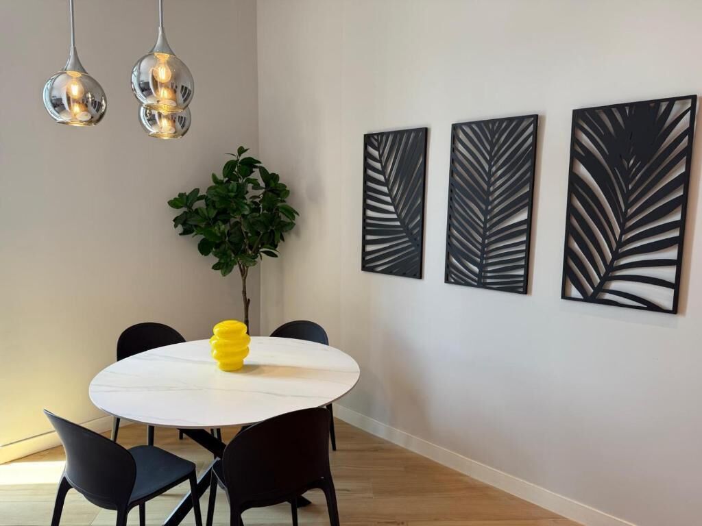 A dining area with a round table, black chairs, a potted plant, and three leaf-patterned wall art pieces.