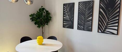 A dining area with a round table, black chairs, a potted plant, and three leaf-patterned wall art pieces.