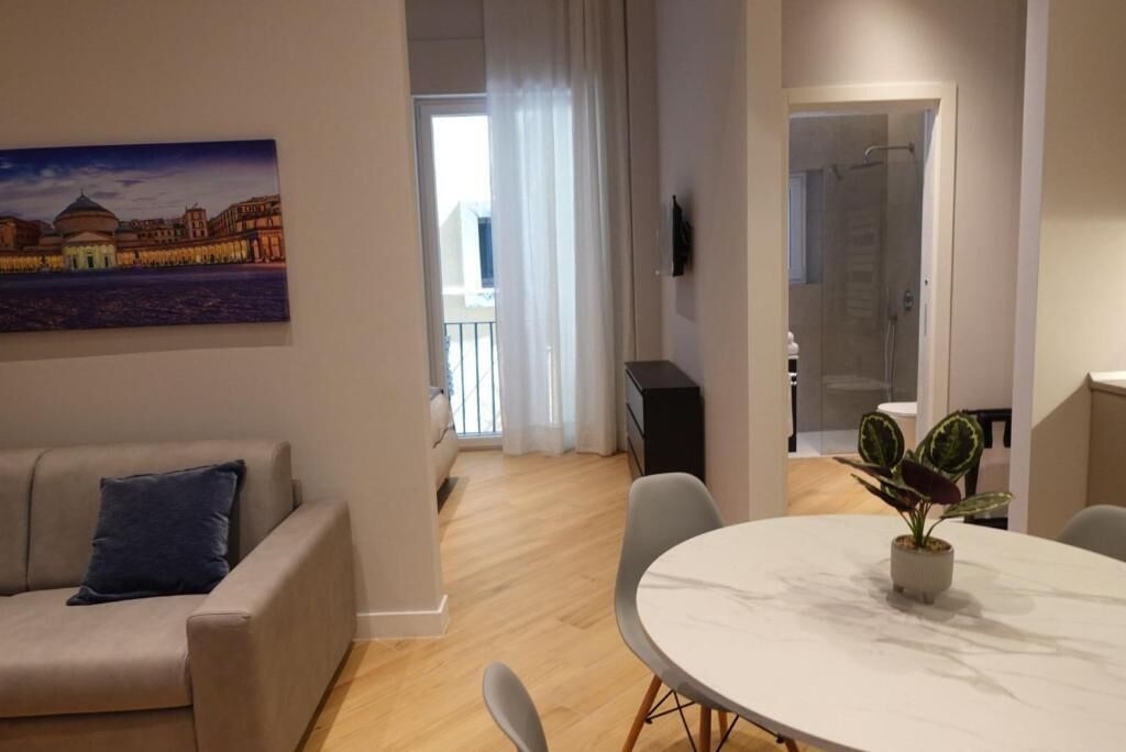 A modern living room with a sofa, a dining table with chairs, a potted plant, and a painting on the wall.